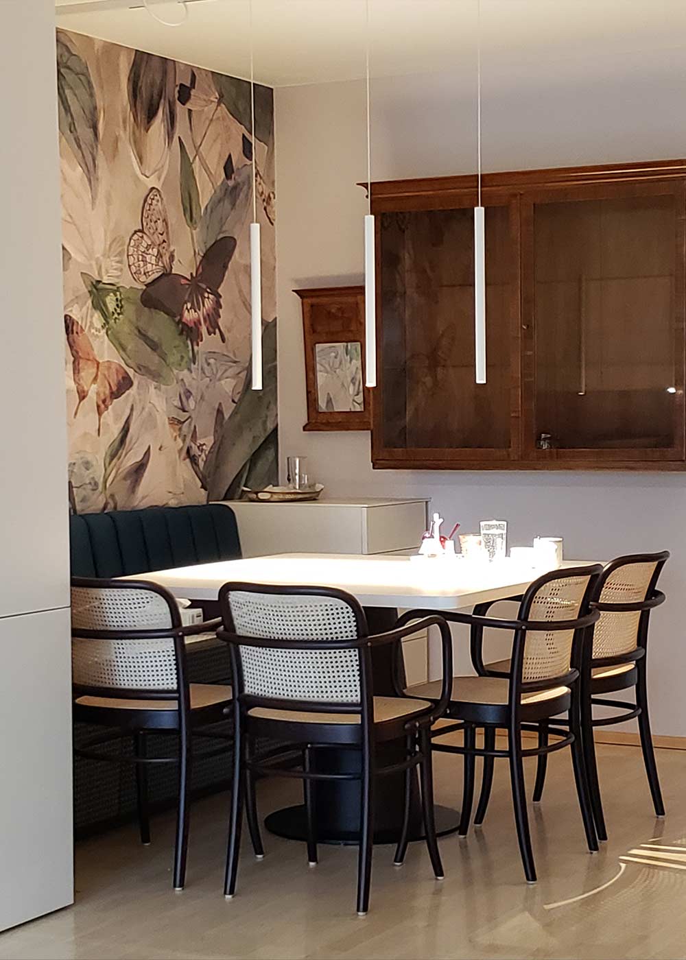 Essbereich mit Tisch, Sitzbank und Hängelampen unter einer Treppe.
